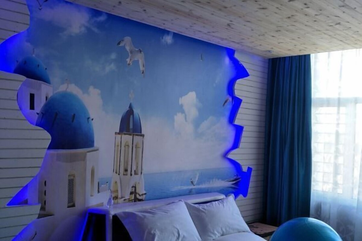 A room with a mural of a coastal scene, a bed, and a window with curtains.