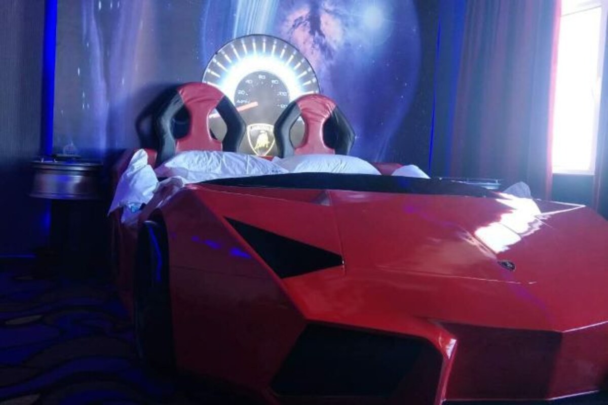 Un letto a forma di auto sportiva rossa con un poggiatesta a forma di contachilometri, un cuscino e una coperta.