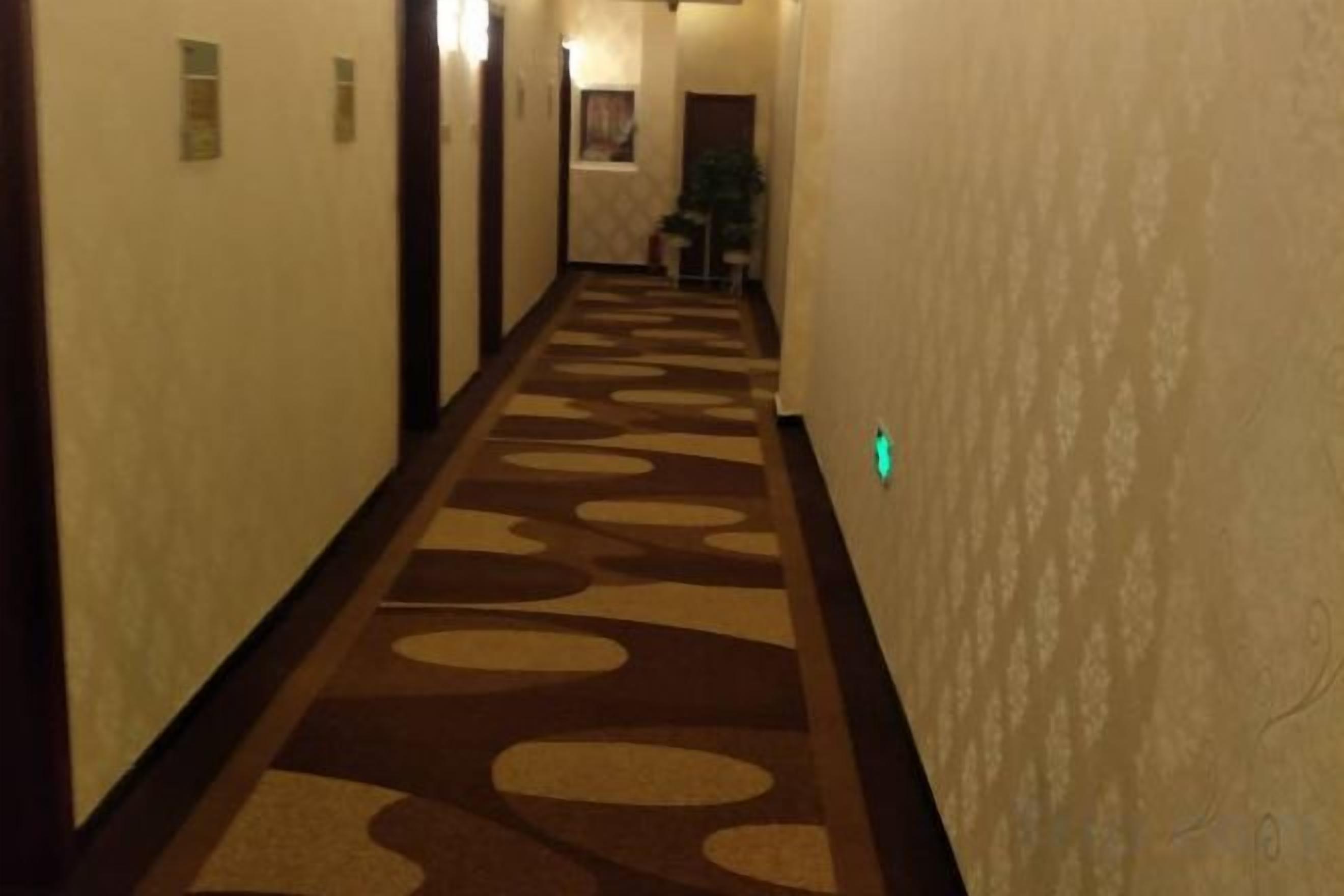 Pasillo de hotel con alfombra estampada, puertas y un letrero de salida verde.