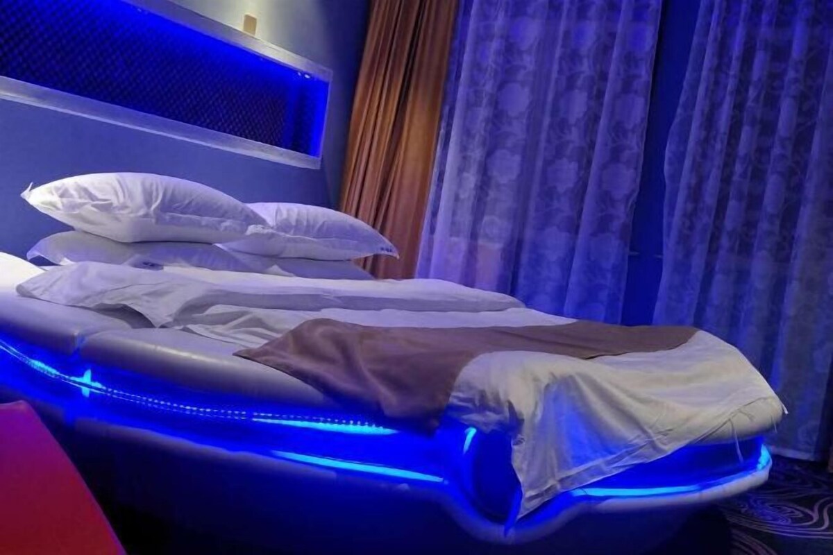 A massage chair with blue LED lights, a bed with pillows, and a curtain in the background.