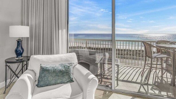 Un balcón con una silla blanca y una mesa, con vistas a una playa y un cielo despejado.