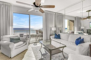 A spacious living room with a glass coffee table, white sofas, and a view of the ocean.