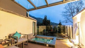 A modern outdoor area with a glass-enclosed hot tub, wooden deck, and a seating area with cushions. - Thinking Land Lingyan Forest Hotel (Dujiangyan)