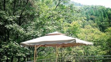 A balcony with a table and chairs, surrounded by lush greenery and a mountainous backdrop.