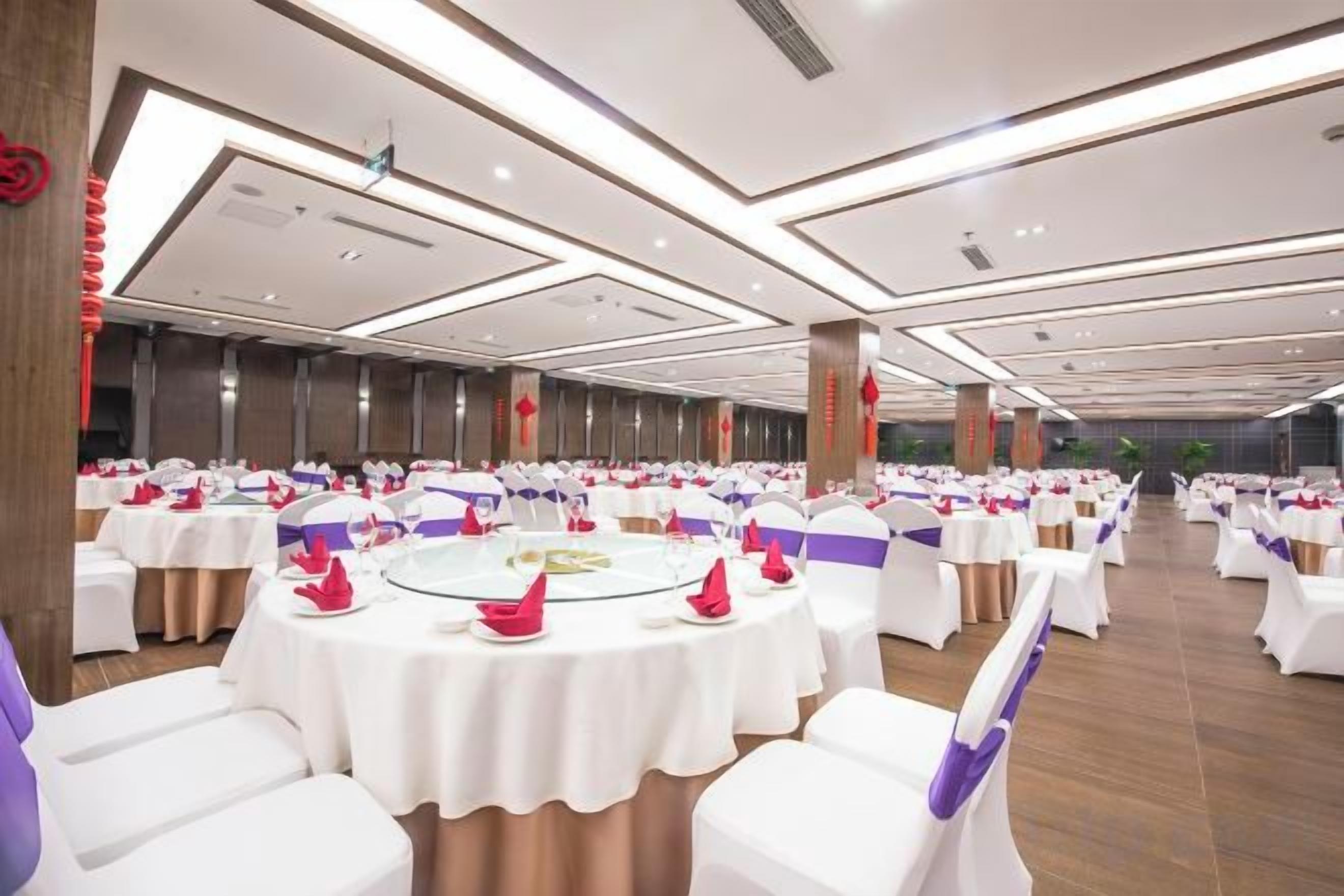 Un salón de banquetes con mesas redondas, manteles blancos y cintas púrpuras.