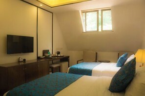 Ein Hotelzimmer mit zwei Betten, einem Schreibtisch, einem Fernseher und einem Fenster, das für natürliches Licht sorgt.