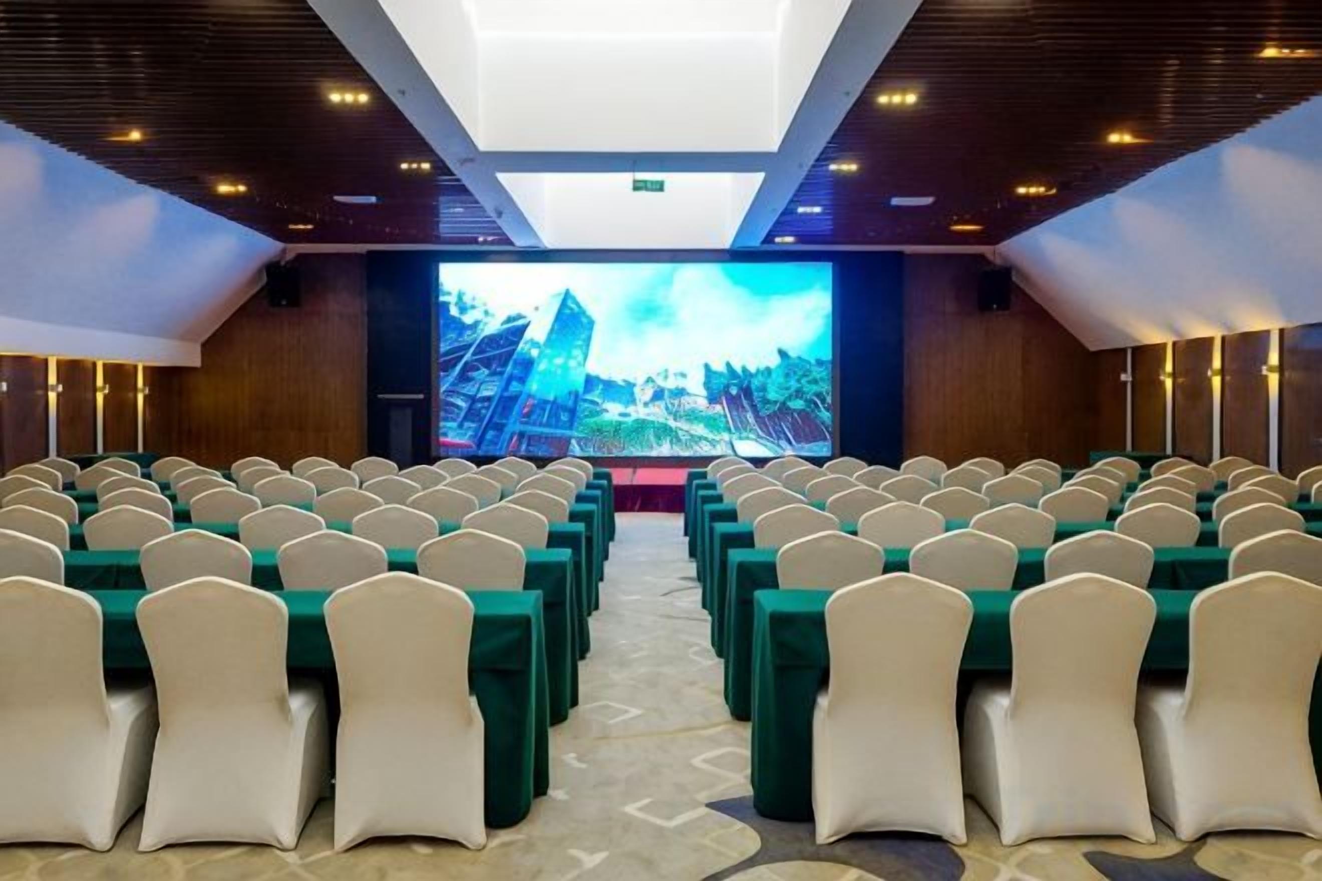 A conference room with rows of chairs and a large screen at the front.