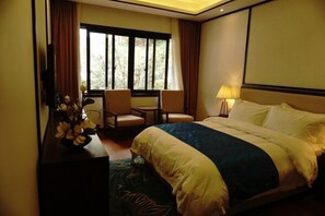 Ein Hotelzimmer mit einem großen Bett, zwei Sesseln, einem Schreibtisch mit Lampe und einem fenster mit Vorhängen.