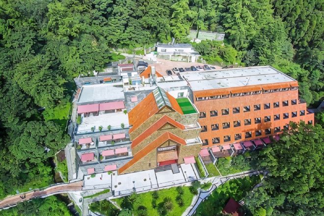 A multi-story building with a unique angular roof design, surrounded by dense greenery.