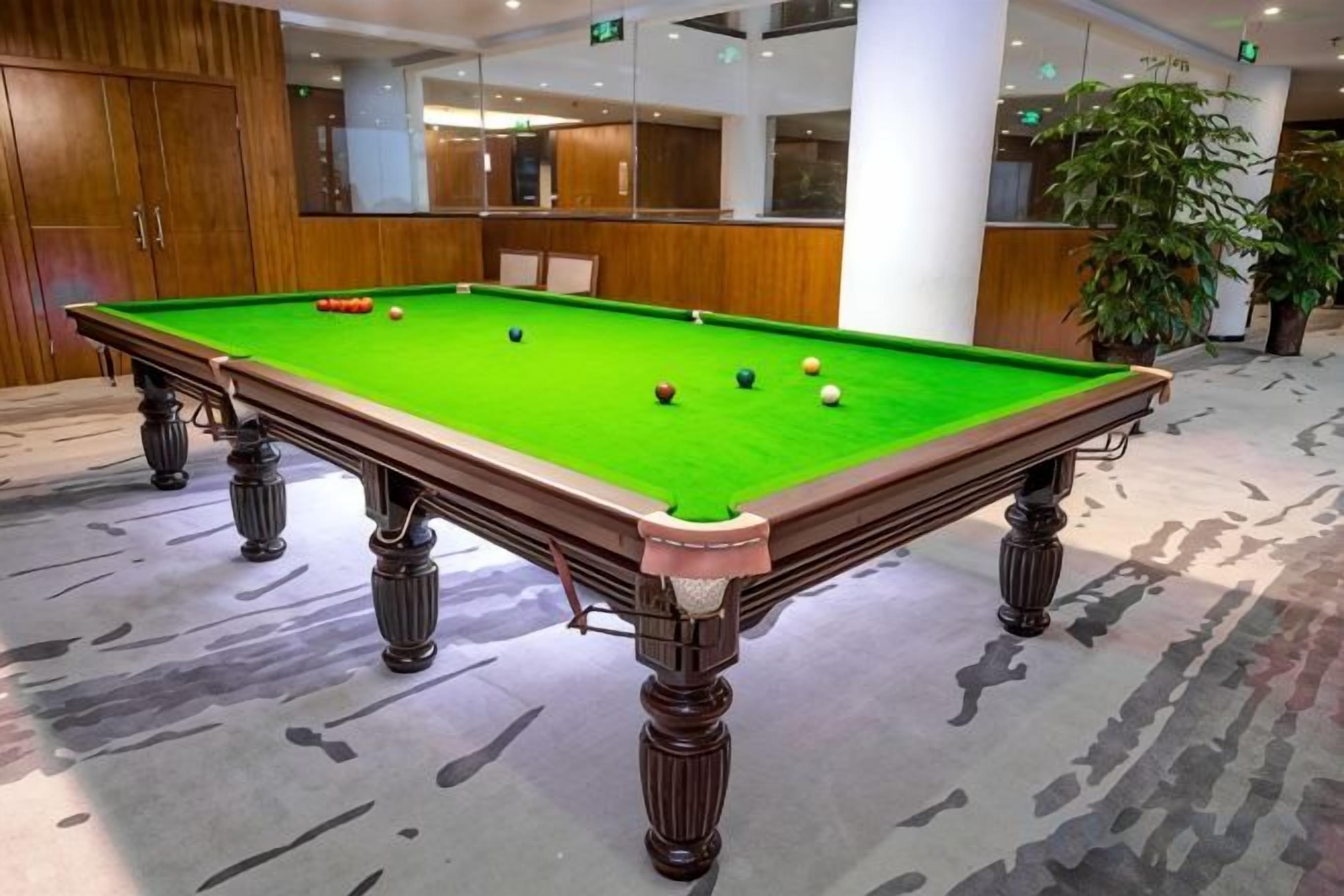 A pool table with balls in a room with wooden cabinets and a large plant.