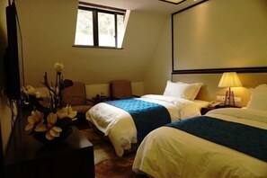 Ein Hotelzimmer mit zwei Betten, einem Schreibtisch mit Blumenvase, einem Fernseher und einem Fenster.