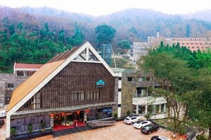 A large building with a sloped roof, a prominent entrance, and a parking area with cars. - Thinking Land Lingyan Forest Hotel (Dujiangyan)