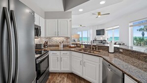 A modern kitchen with white cabinets, stainless steel appliances, a granite countertop, and a view of the ocean.
