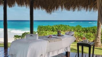 Relax in a serene oceanfront setting with a comfortable bed, wooden deck, and lush greenery.