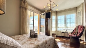 Un dormitorio con una cama grande, una silla y vistas al exterior a través de amplios ventanales.