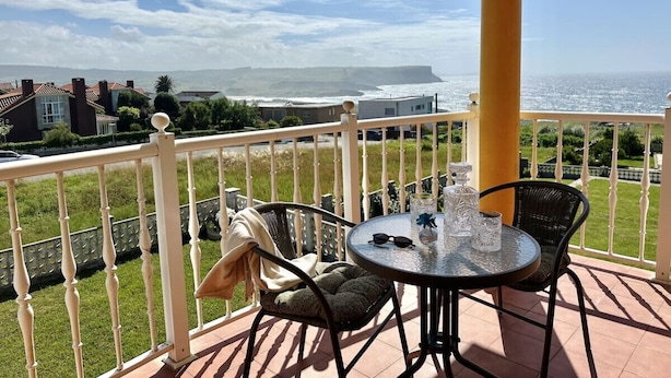 Un balcón con una mesa y sillas, con vistas a la costa, casas y un acantilado.
