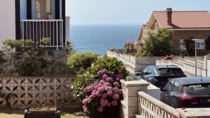 Zona residencial costera con vista al mar, un balcón con barandilla y coches aparcados.