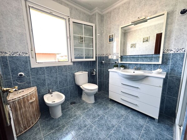 Un baño con inodoro, bidé, tocador con espejo y un armario de madera.