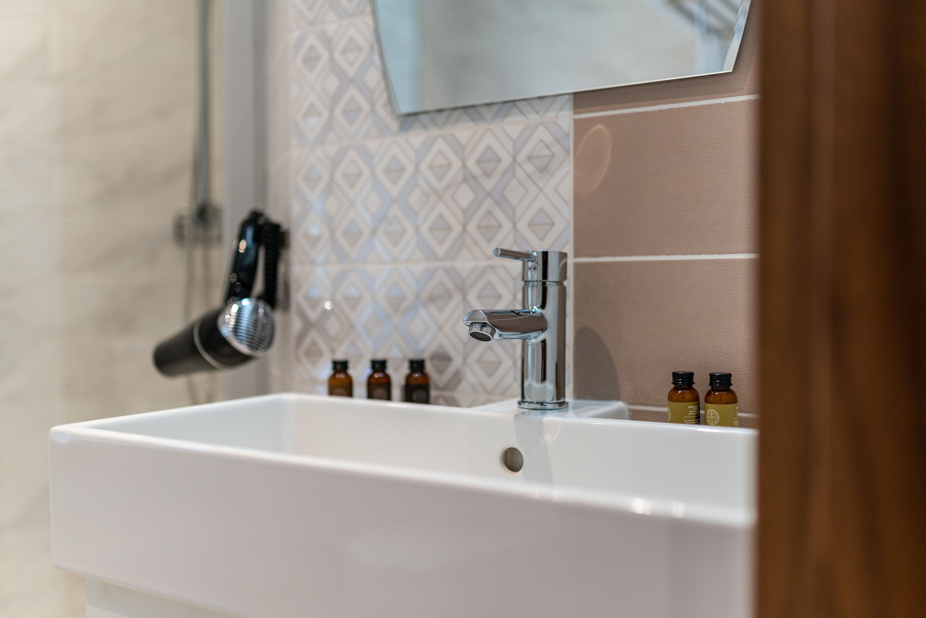 A bathroom with a white sink, a mirror above it, and a towel rack. There are three small bottles on the sink.