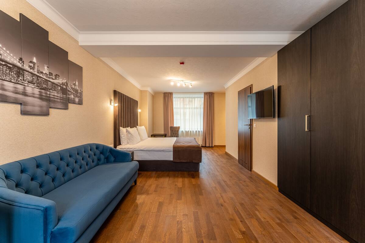 A hotel room with a large bed, a blue sofa, a flat-screen TV, and a cityscape painting on the wall.