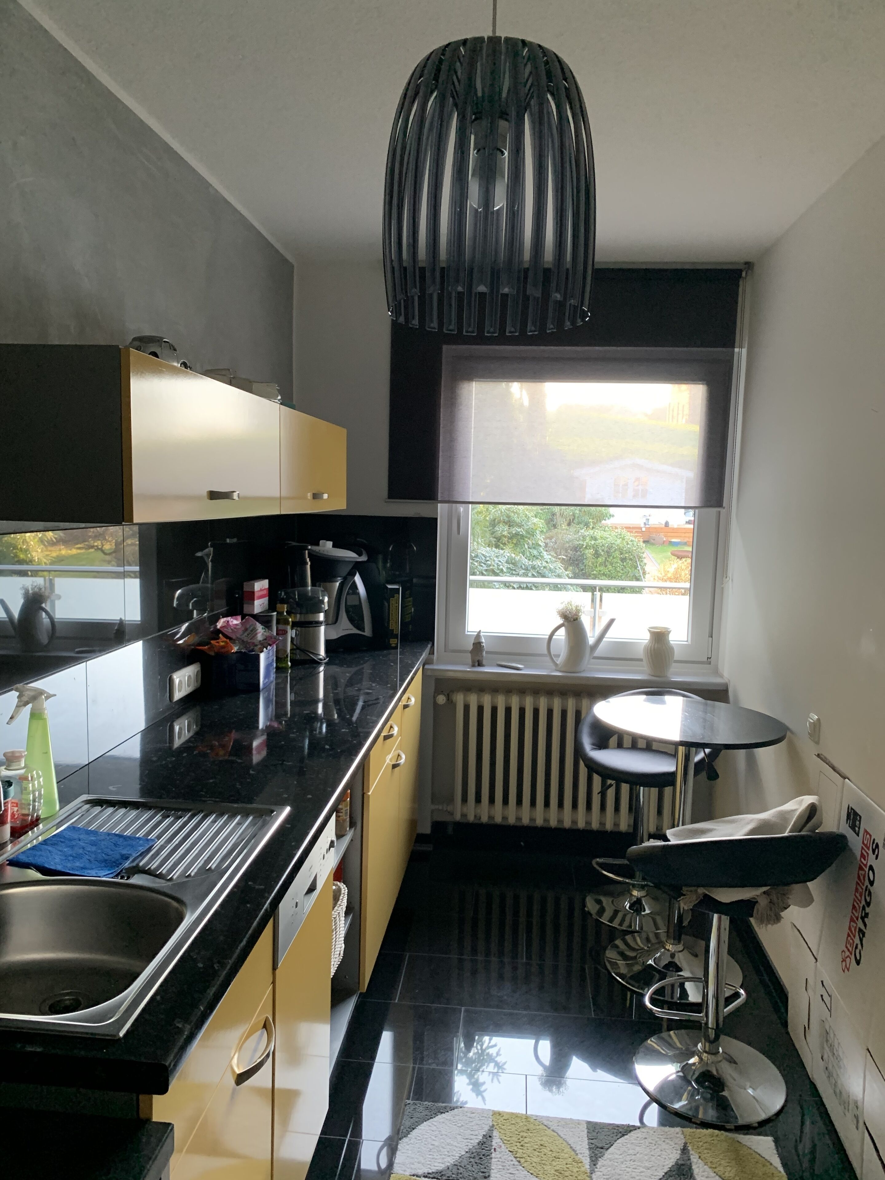 Een moderne keuken met een zwart aanrecht, een roestvrijstalen spoelbak en een raam met uitzicht op groen.