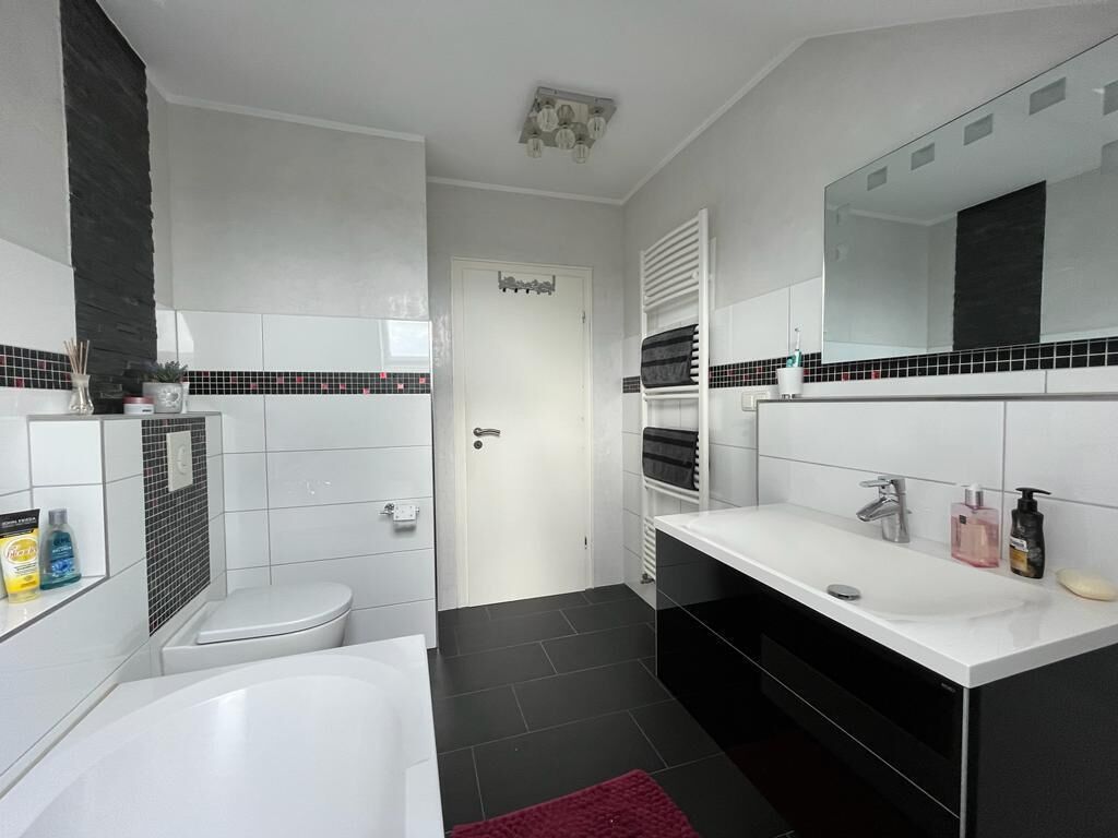 Un bany modern amb una banyera blanca, un mirall gran i un lavabo blanc amb armaris negres.