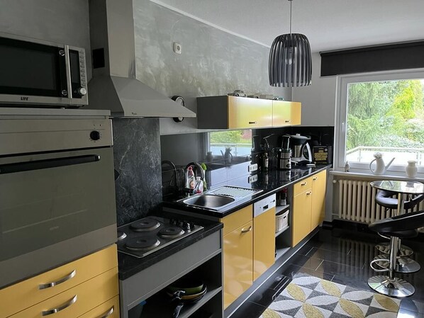 A modern kitchen with stainless steel appliances, yellow cabinets, and a black countertop. - Beautiful vacation apartment in Essen-Burgaltendorf (Essen)