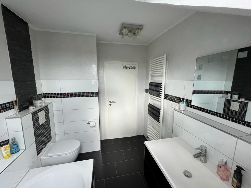 Une salle de bain moderne avec des toilettes blanches, une baignoire et un lavabo agrémenté d’un miroir.