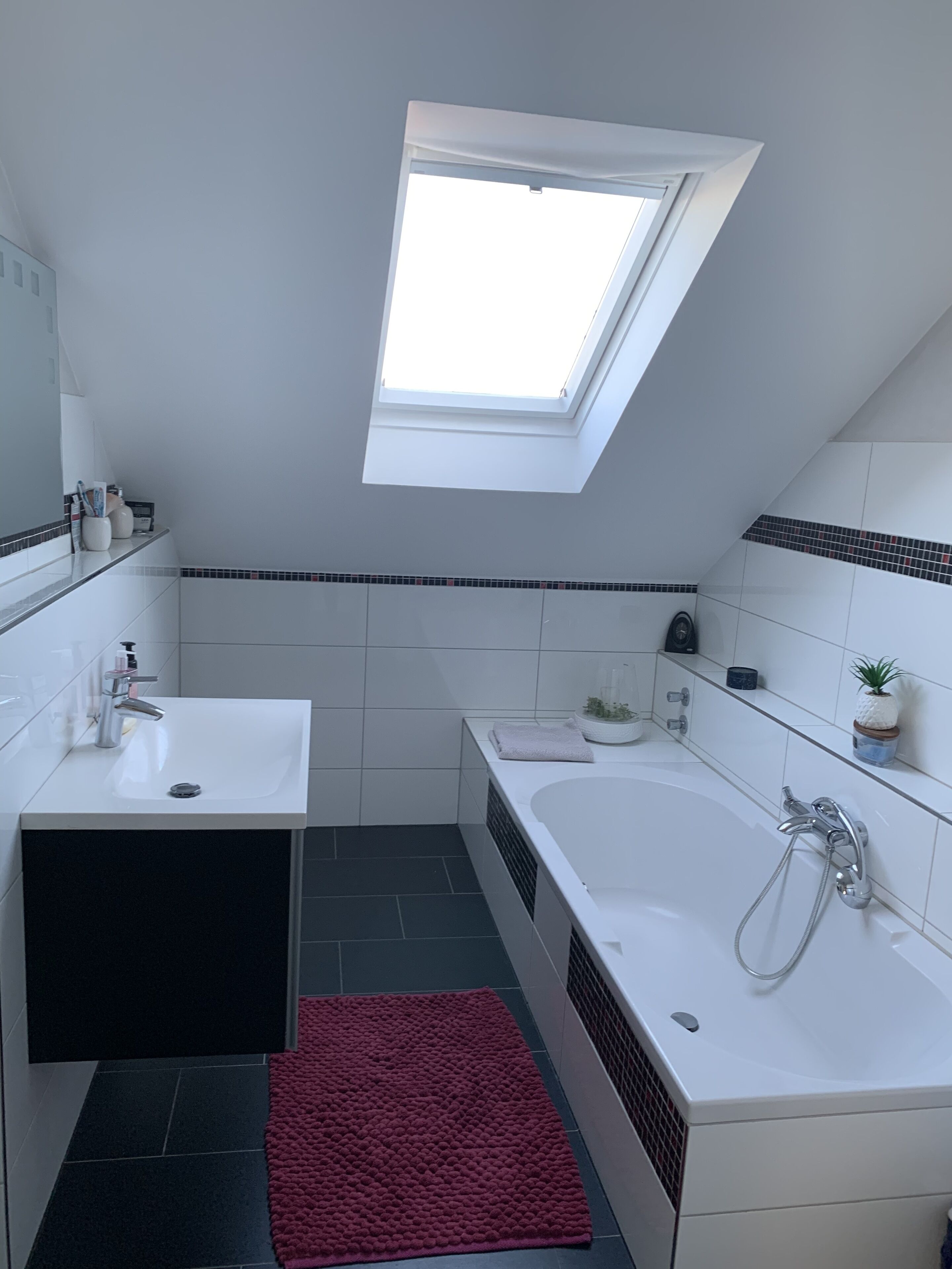 Un baño moderno con tragaluz, una bañera, un lavabo y una alfombra roja.