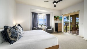 A bedroom with a bed, a ceiling fan, a view of the outdoors, and a sliding door leading to a balcony.