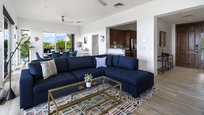 A modern living room with a sectional sofa, a glass coffee table, and a view of the kitchen and dining area.
