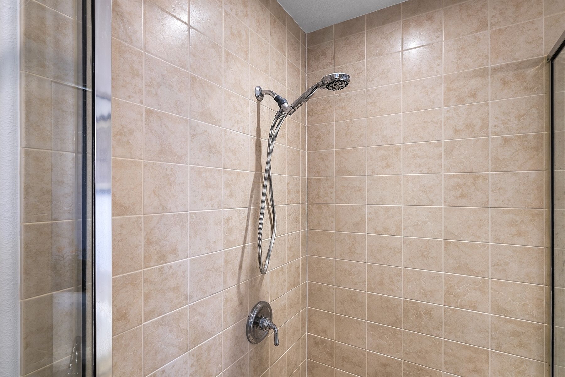 A shower with a handheld showerhead and a wall-mounted faucet.