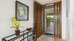 A hallway with a wooden door, a map on the wall, a potted plant, and a metal console table.