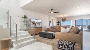 Un espacio habitable amplio con una escalera moderna, un conjunto de sofás cómodo y una pantalla de televisión grande.