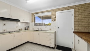 A kitchen with white cabinets, a black countertop, a sink, and a window with a view of trees. - Ocean Drift - short stroll to cafes/restaurants and beaches (Woolgoolga)