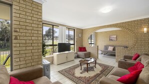 A living room with a brick wall, a TV, a sofa, a coffee table, and a rug. - Ocean Drift - short stroll to cafes/restaurants and beaches (Woolgoolga)