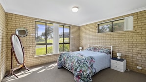 A bedroom with a brick wall, a large window, a bed, a bedside table, and a mirror. - Ocean Drift - short stroll to cafes/restaurants and beaches (Woolgoolga)