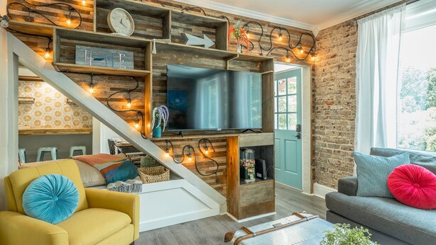 A modern living room with a TV mounted on a wooden wall, a staircase with a light fixture, and a cozy seating area with a sofa and armchairs. - WALK to top Chattanooga action from this Fun Fabulous Family/Friend(ly) Home! (Chattanooga)