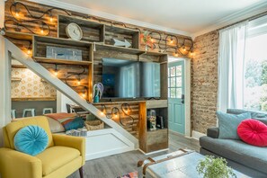 Una sala de estar moderna con un televisor montado en una pared de madera, una escalera con una lámpara y una zona de estar acogedora con un sofá y sillones.