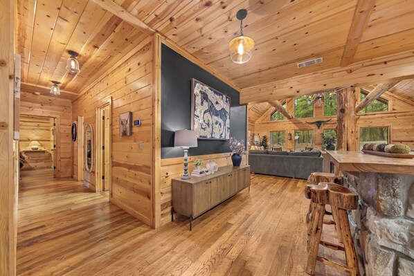 A log cabin interior with a dining area, a living room with a sofa, and a kitchen area.
