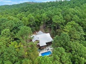 A secluded cabin surrounded by dense forest, featuring a swimming pool and a deck area.