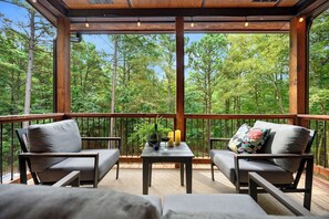 A wooden deck with two grey sofas and a table, surrounded by a forest view. - Family Fun | Pool | Near State Park | Secluded (Broken Bow)