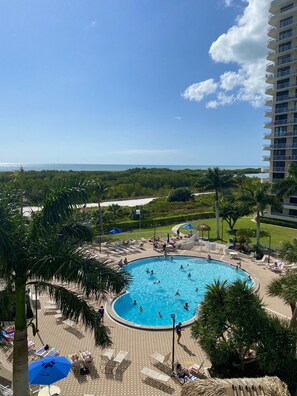 A pool area with lounge chairs and umbrellas, surrounded by greenery and a view of the ocean.