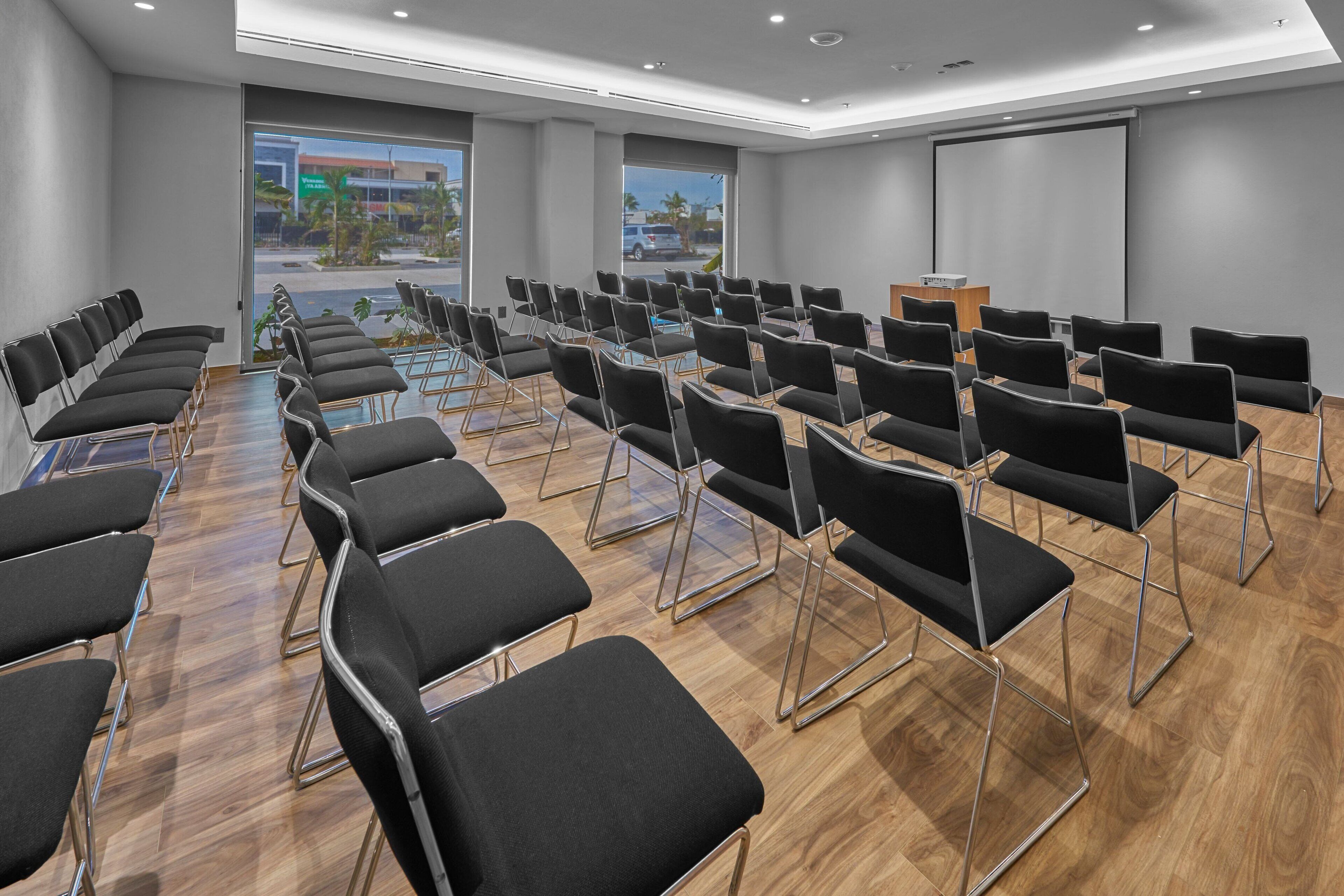 A conference room with rows of black chairs, a podium, and a large screen.