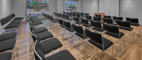 Un salón de conferencias con filas de sillas negras, un atril y una pantalla grande.
