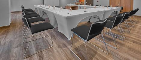 Una sala de conferencias con una larga mesa, sillas negras y botellas de agua.