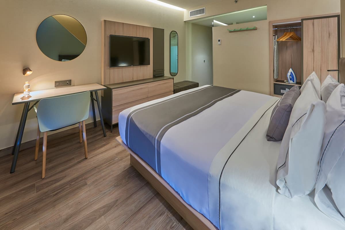 A modern hotel room with a bed, desk, chair, and a TV.