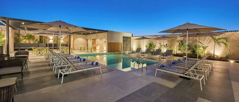 A pool area with lounge chairs and umbrellas, surrounded by potted plants and a modern building facade.