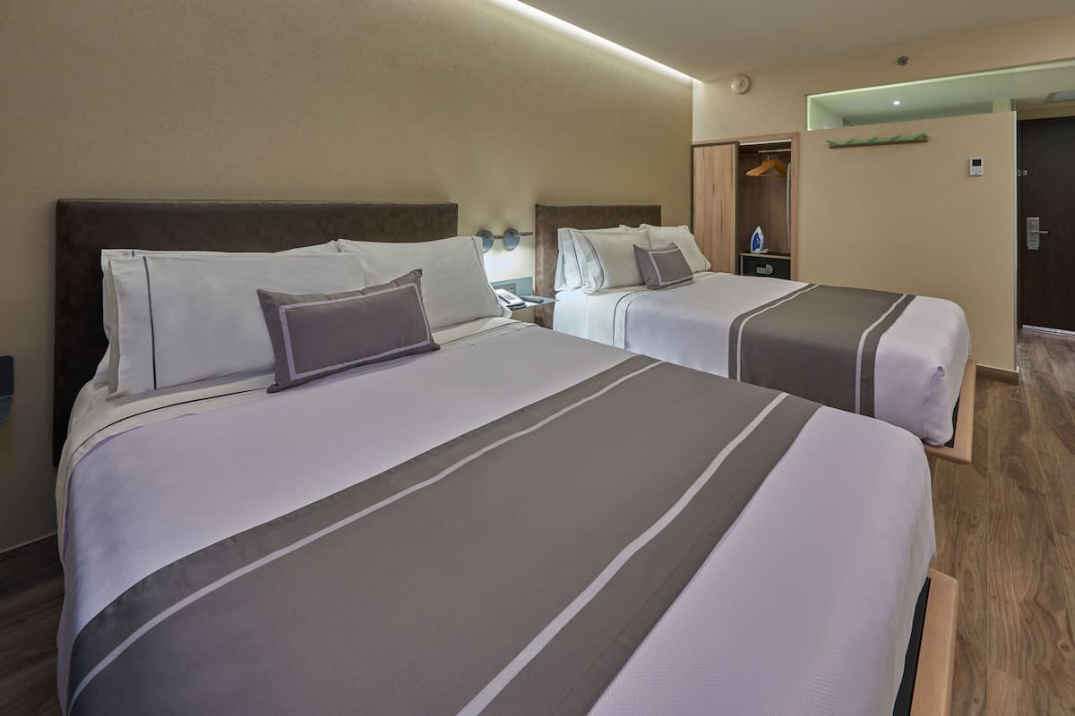 A hotel room with two beds, each with a headboard, a nightstand, and a wardrobe.