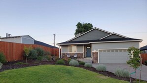 A single-story house with a garage, a front yard with a lawn and shrubs, and a wooden fence. - This house is a 4 bedroom(s), 2 bathrooms, located in Eagle Point, OR. (Eagle Point)